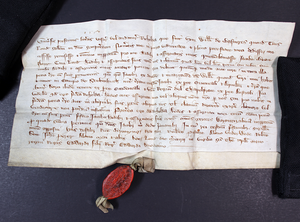 A handwritten document held down with black weights with an ornate oval red wax seal at the bottom.