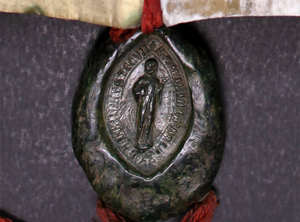 A dark, mottled, oval-shaped seal showing a human figure surrounded by words attached to red string.