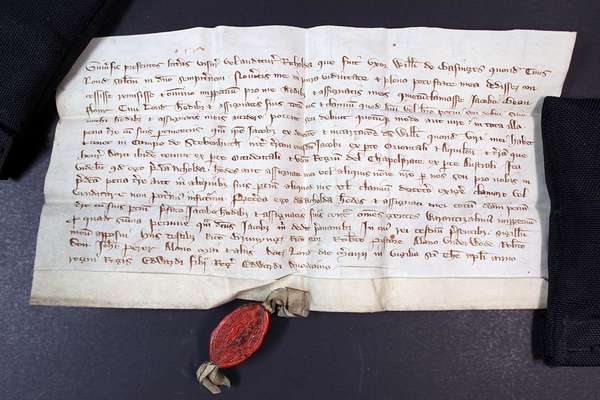 A handwritten document held down with black weights with an ornate oval red wax seal at the bottom.