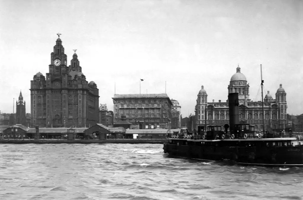 A ship sailing away from three large buildings on land.