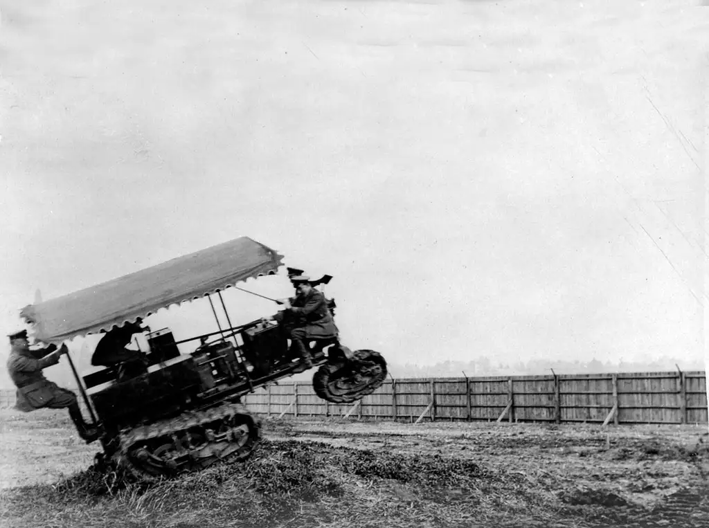 A photograph of an early tank moving a fast speed over a bump with people inside.