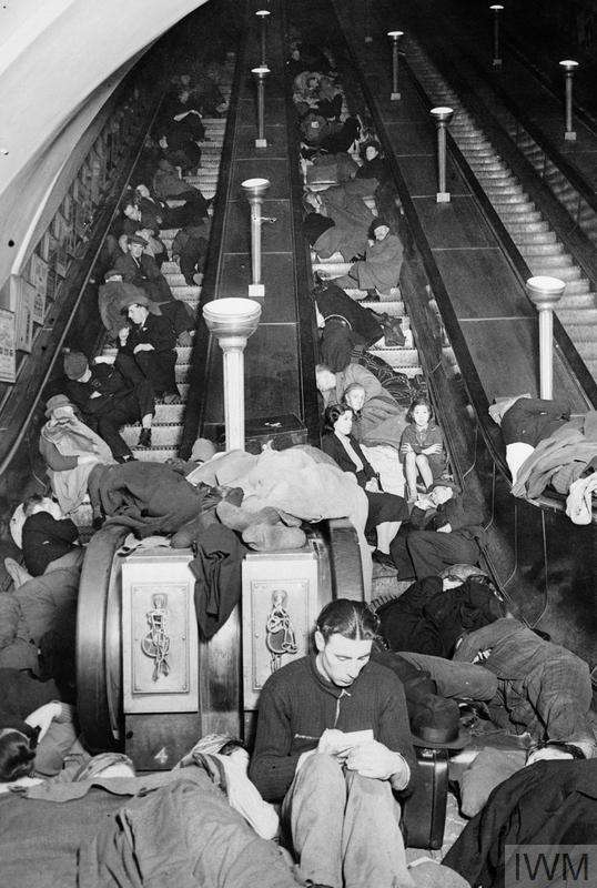 People, young and old, on the steps, the floor and the base of an escalator trying to sleep.