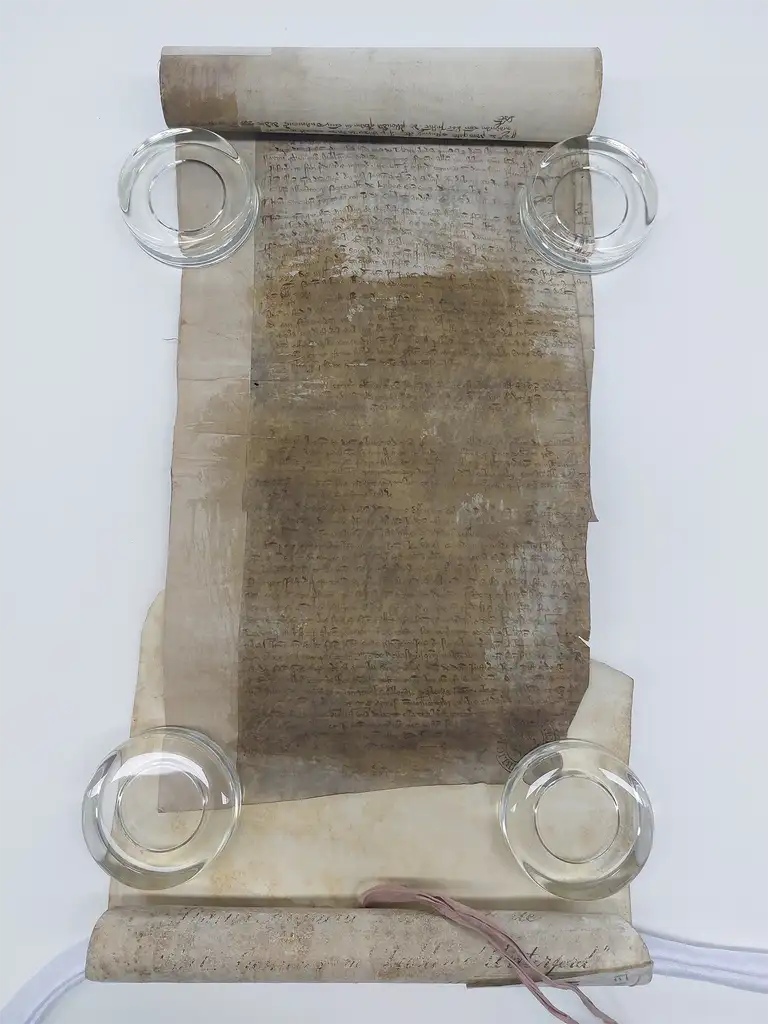 A medieval roll laid out on table. It's handwritten but most of the writing is blocked by a stain.