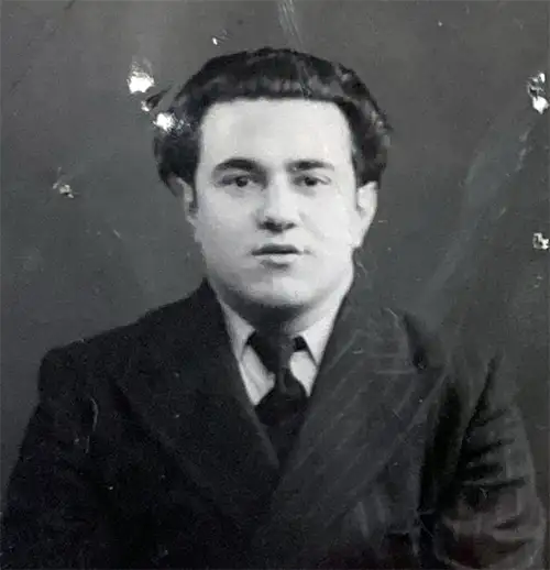 A passport-style photograph of a seated man wearing a suit and tie.