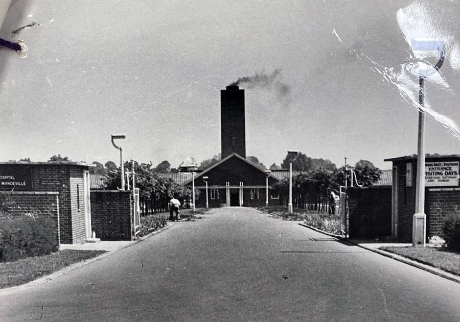 A black and white photograph of the road leading to an entrance of Stoke Mandeville Spinal Unit.