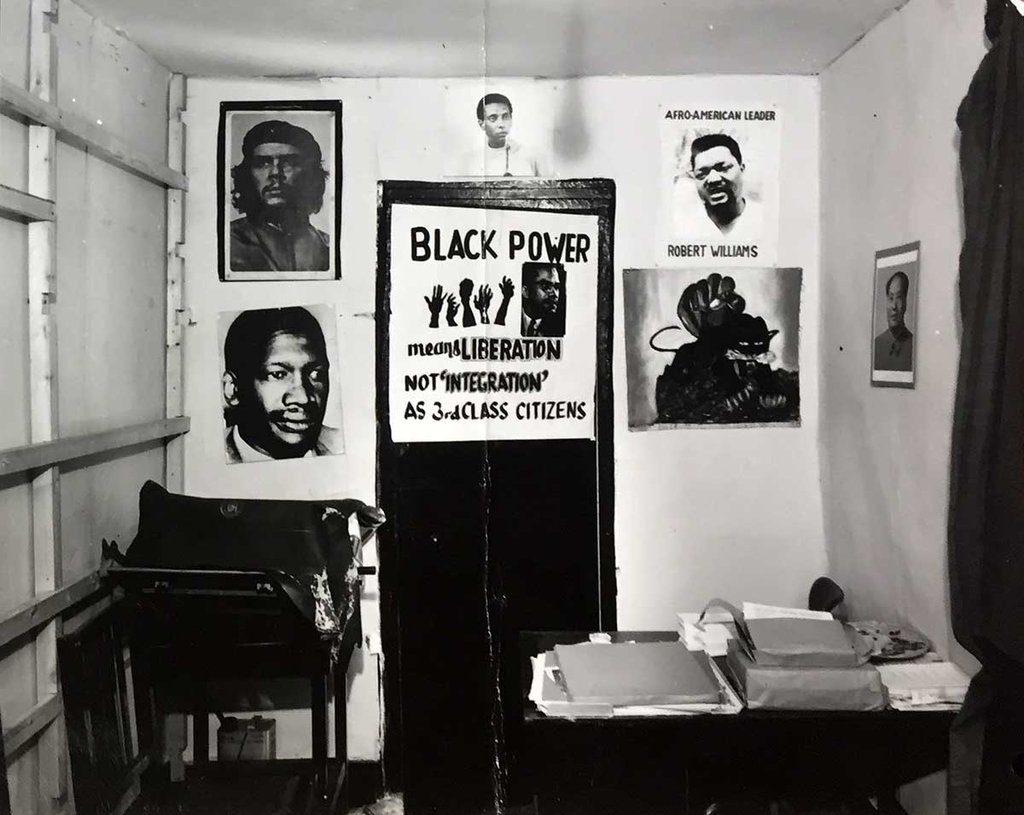A small, cramped room with a desk covered in files and lots of civil rights posters on the wall.