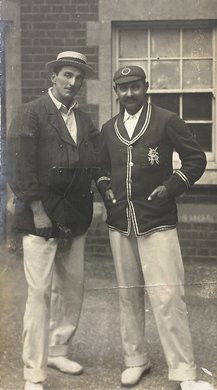 Two cricket players wearing smart cricket attire standing outside.