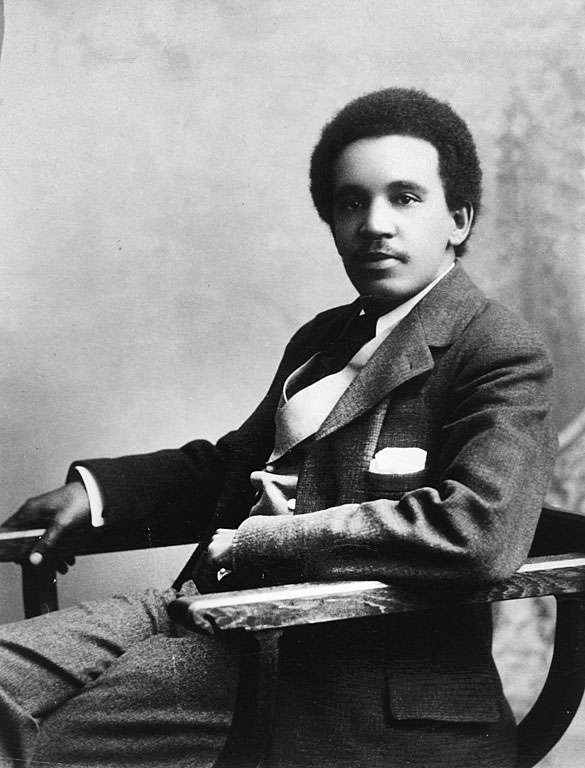 Photograph of young mixed-heritage man in a smart suit sitting casually in a chair