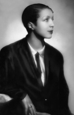 Black and white photo of Evelyn, seated, wearing a suit and tie and with a short hairstyle.
