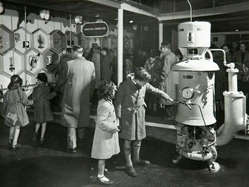 Visitors look at displays on a wall. In the foreground two children look at a robot