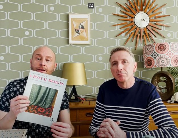 Two men sit in a 1950's style room. One holds up a document