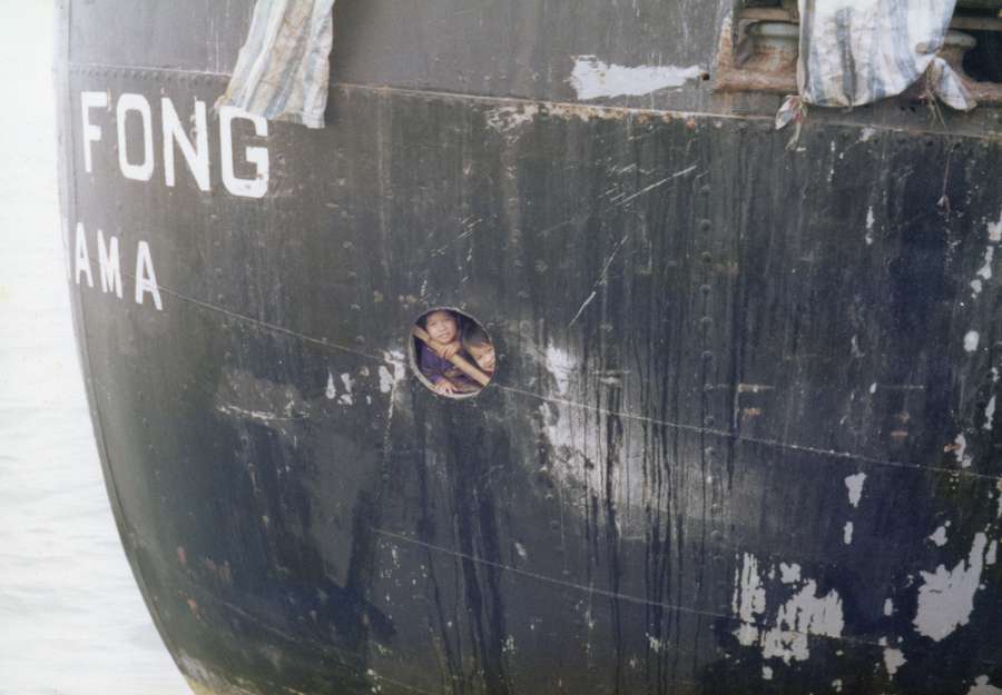 Two young refugees look out of small rounded window aboard the Huey Fong.