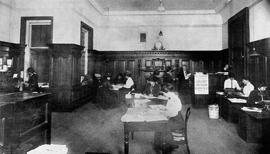A group of women working at desks in a large wood-panelled office.