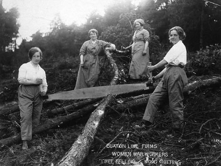 Four women stand over a fallen tree, two of them holding an enormous saw between them.