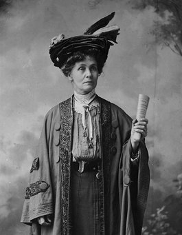 A photographic portrait of Emmeline Pankhurst. She is confidently holding out a rolled up document.