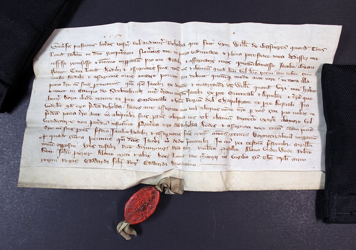 A handwritten document held down with black weights with an ornate oval red wax seal at the bottom.