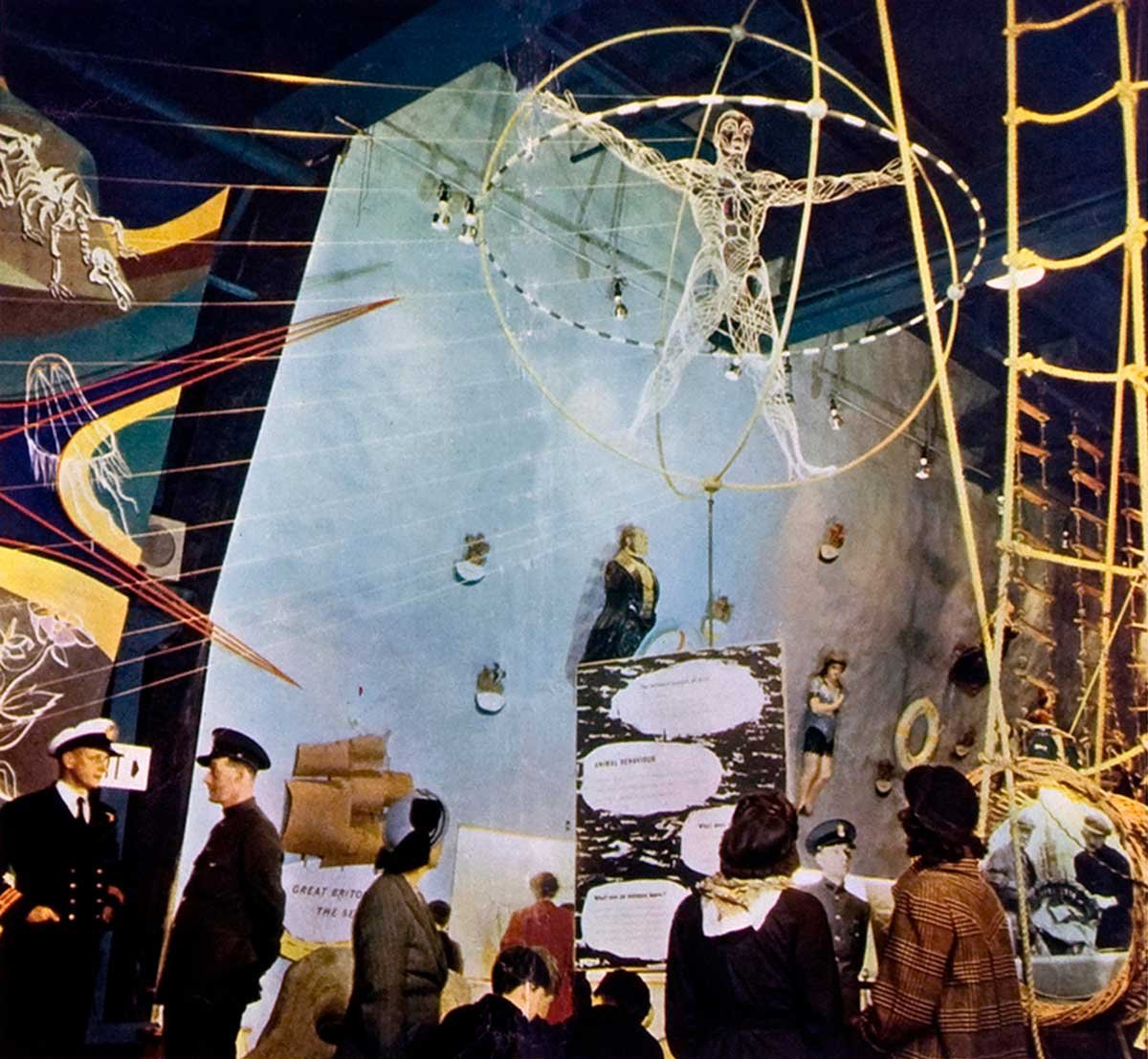 Visitors look at a model of a muscular human form surrounded by gold rings and other exhibits.