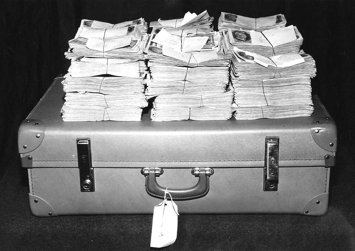 Photograph of a suitcase with piles of money on top of it
