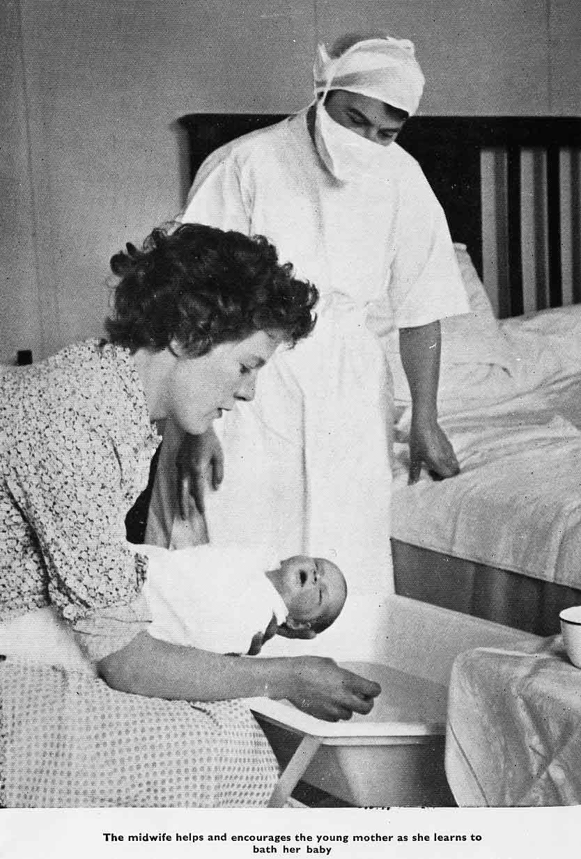 A woman in a blouse sits holding a tiny baby below a woman in a white gown and mask.