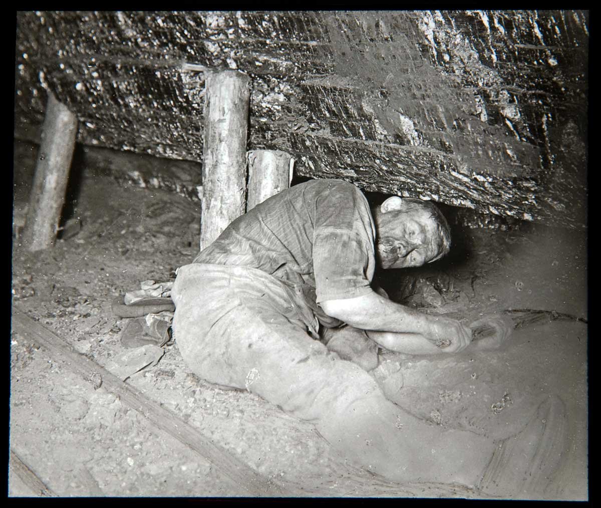 A man lying down under a supported section of cave holding a tool in both hands.