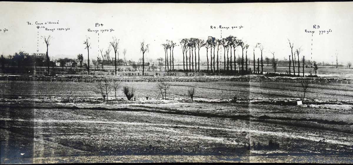 Landscape photo showing bare fields with trenches dug in, and a row of thin trees.