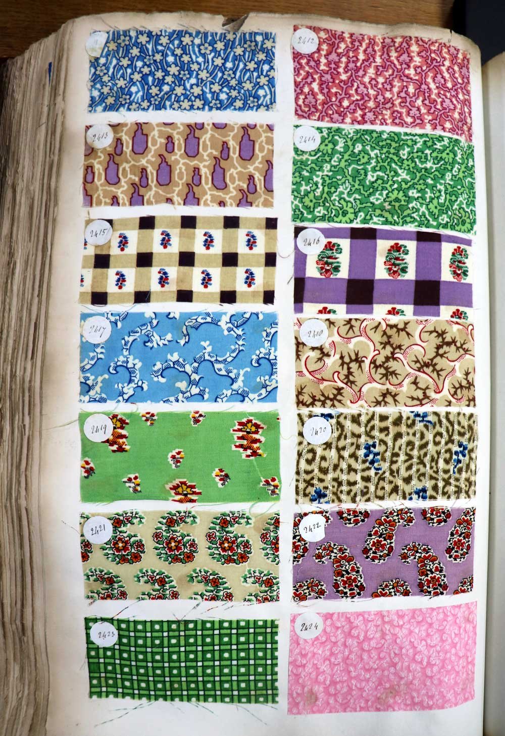 Fourteen small, rectangular patches of textiles showing very different colourful patterns.