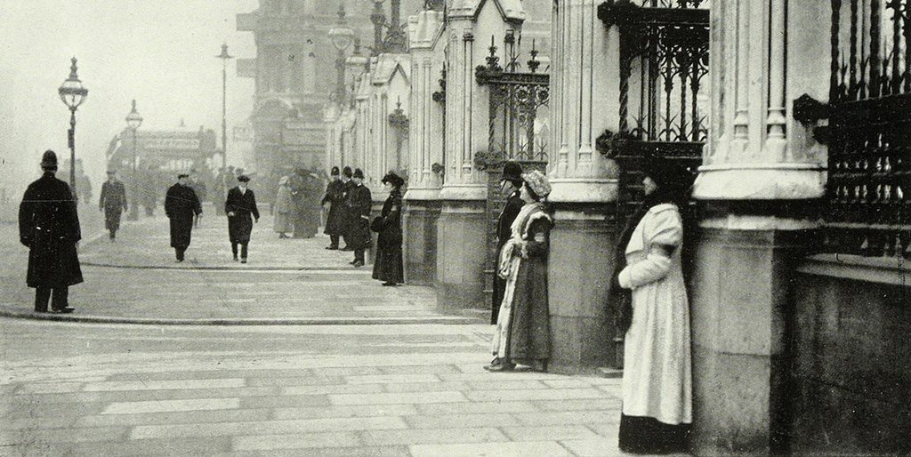 A photo of two women standing besides pillars outside the House of Commons. Police are watching on.