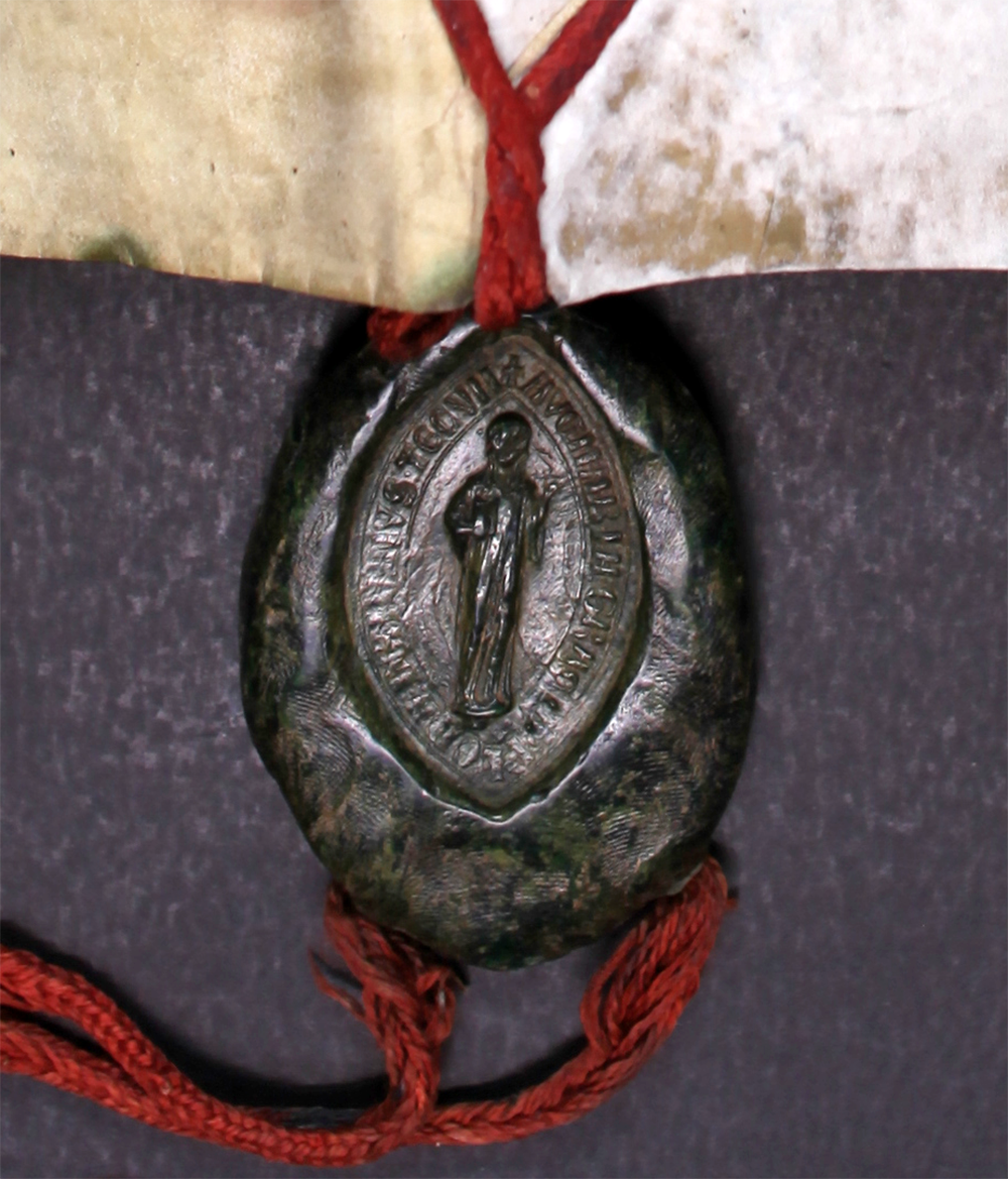 A dark, mottled, oval-shaped seal showing a human figure surrounded by words attached to red string.
