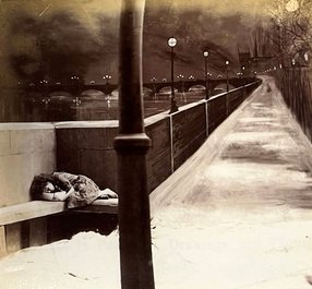 A street scene at night. A girl sleeps in her working clothes on a bench alongside a deserted path