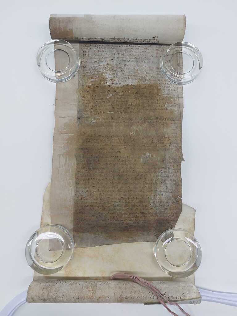 A medieval roll laid out on table. It's handwritten but most of the writing is blocked by a stain.