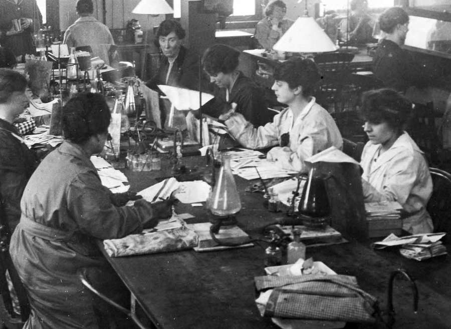 Photograph of women sat around a long table covered with beakers and letters.