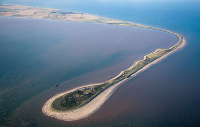 A narrow peninsula of land and beach curving at a right angle, surrounded by water.