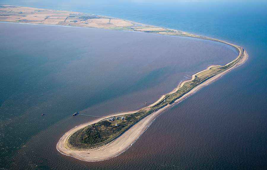 A narrow peninsula of land and beach curving at a right angle, surrounded by water.