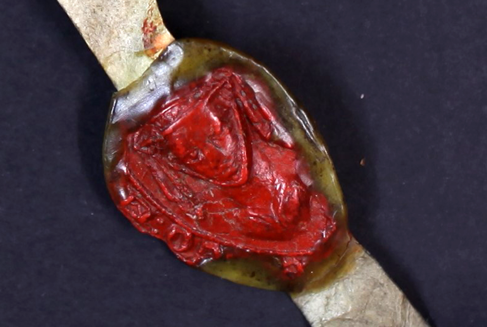 A red wax seal in the shape of a veiled woman's face on a strip of leathery material.