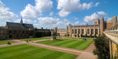 Perfectly-mowed green lawns next to historic stone buildings under a blue sky.