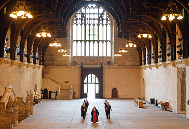 A small procession walks down a grand stone hall with ornate wooden arches.